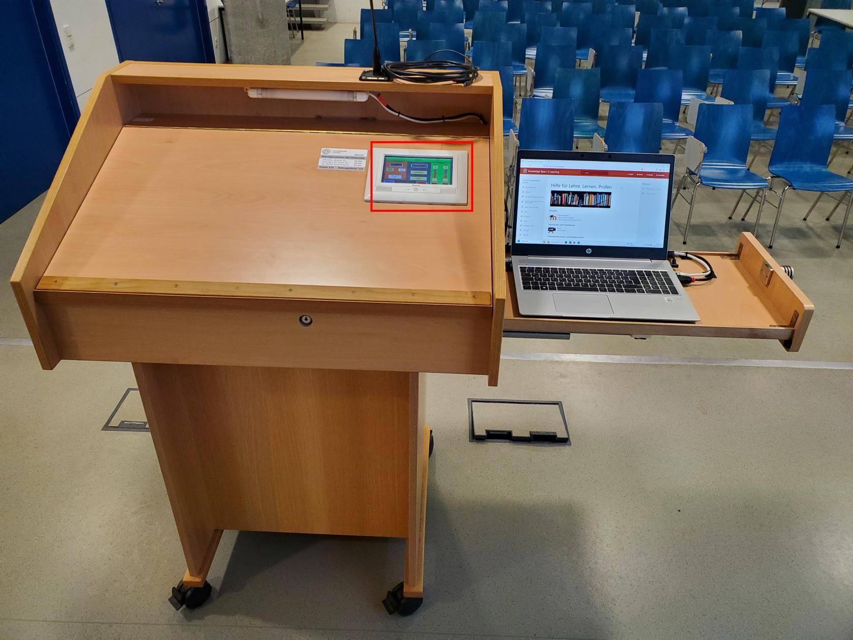 Dozierendenpult mit ausgezogener Laptop-Schublade, in der rechten oberen Ecke der Ablage das eingelassene Raum- und Mediensteuerungs-Touch-Display