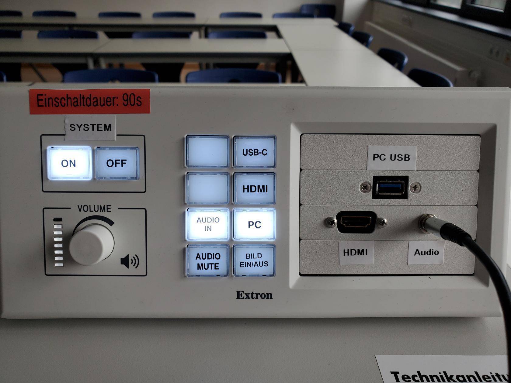 Nahaufnahme des-Mediensteuerung-Panels mit Anschlüssen. In der Klinkenbuchse steckt das Verbindungskabel vom Sennheiser-Empfänger.