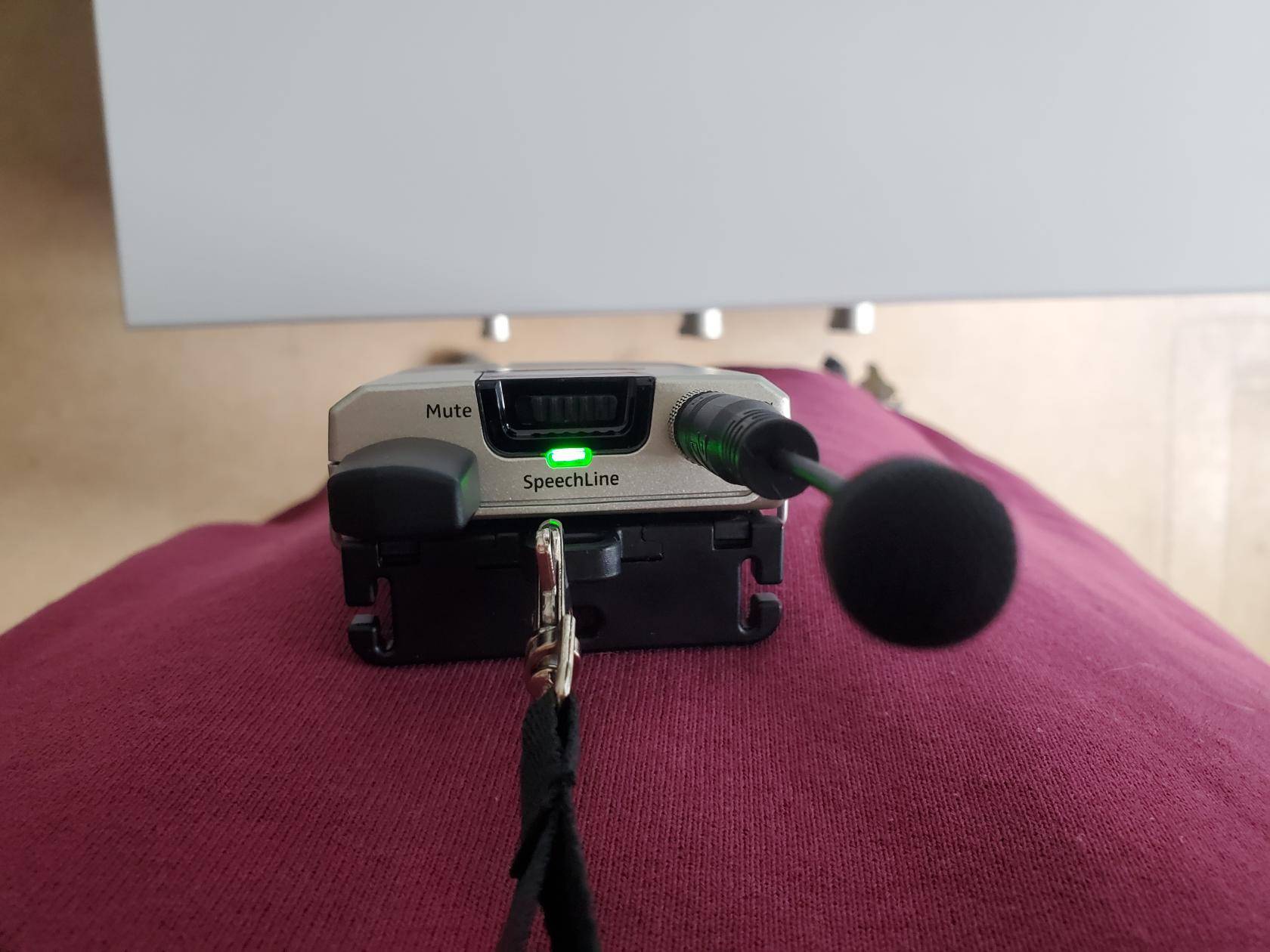 Umgehängte Sendereinheit mit Mikrofon. Die LED an der Oberseite leuchtet grün.